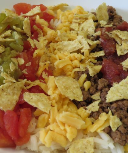 A bowl of white rice topped with hamburger, tomatoes, salsa, green chiles, cheese, and tortilla chips