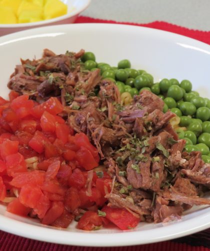 A bowl of ramen noodles with diced tomatoes, beef, peas, and dried chives