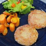 Artichoke cakes on a blue plate with roasted carrots and tossed salad