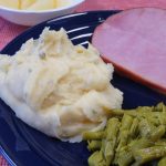 Cheese and chive mashed potatoes on a dinner plate with sliced ham and asparagus