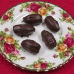 Chocolate covered pecans tuffed date sitting on a china plate