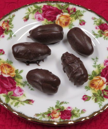 Chocolate covered pecans tuffed date sitting on a china plate