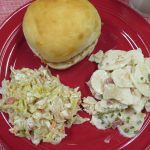 Pulled pork sandwich, pickled cabbage slaw, and Bacon Ranch Potato Salad on a red plate.