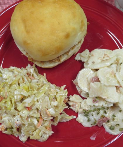Pulled pork sandwich, pickled cabbage slaw, and Bacon Ranch Potato Salad on a red plate.